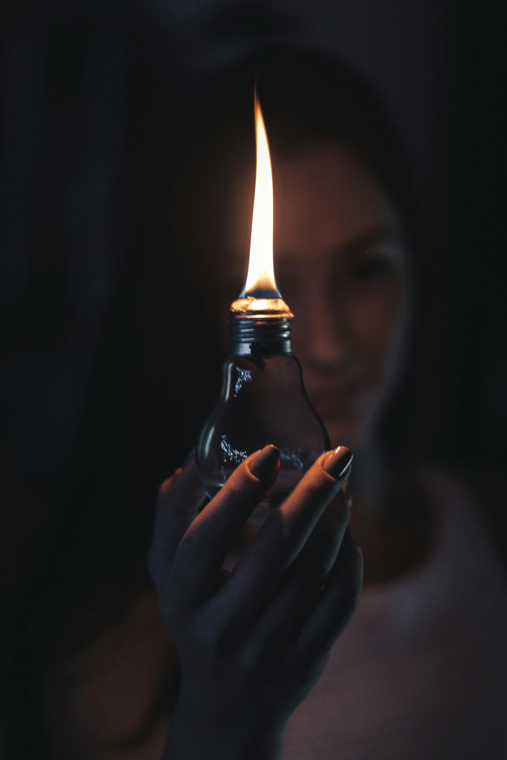 A glowing flame inside a light bulb held by a woman, creating a warm and mysterious ambiance.