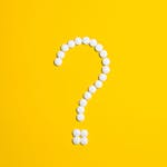 White pills arranged in a question mark shape on a bright yellow background, symbolizing medical queries.