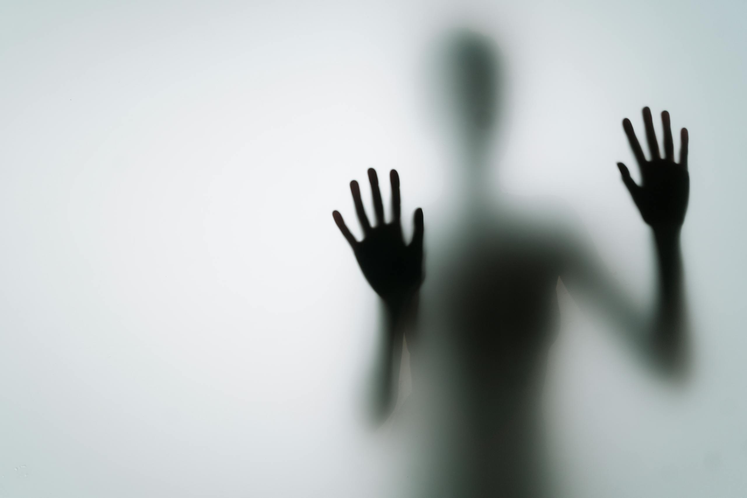 Abstract silhouette of person with hands against glass, creating a mysterious vibe.