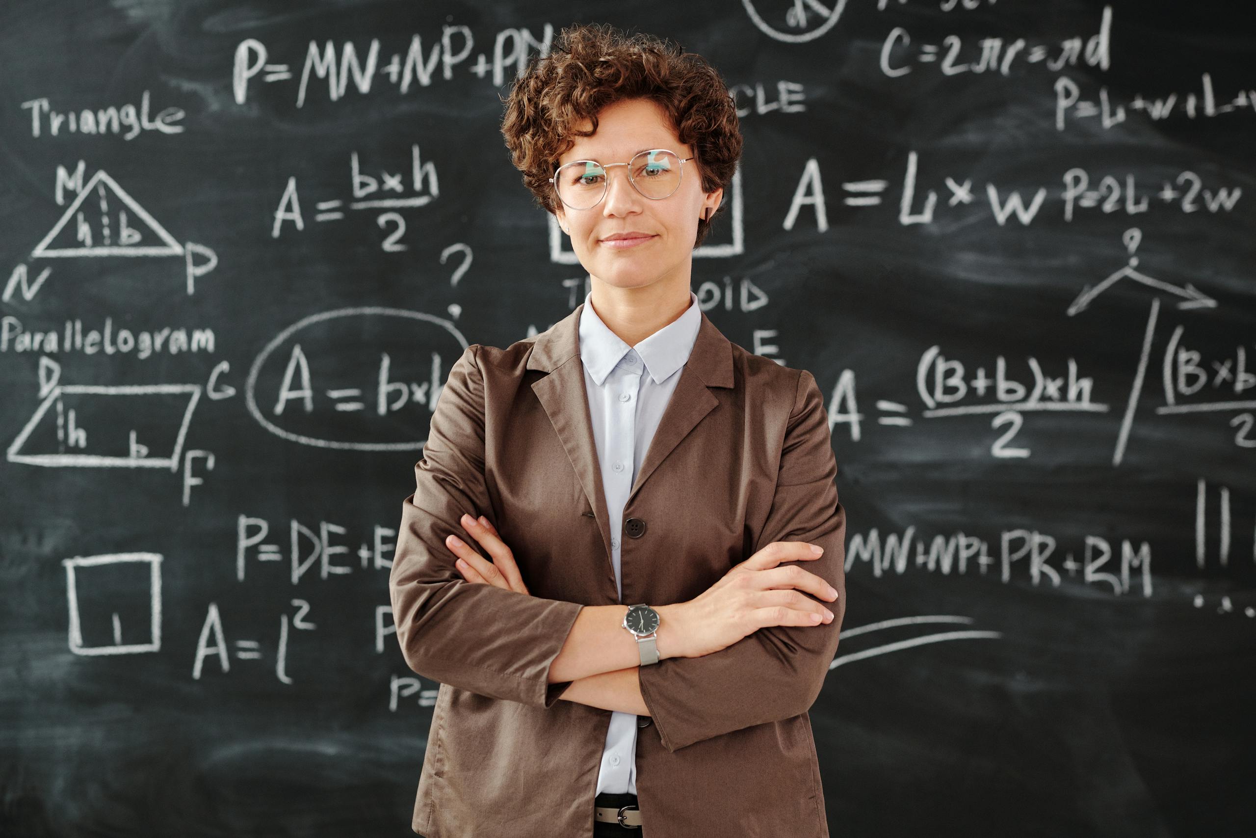 Confident female teacher standing with arms crossed in front of a detailed mathematical blackboard.