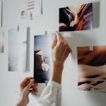Hands arranging a mood board with various photos on an indoor wall.