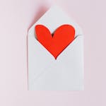 Top view of opened white envelope with handmade red paper heart placed against pink background as gift for Valentine day