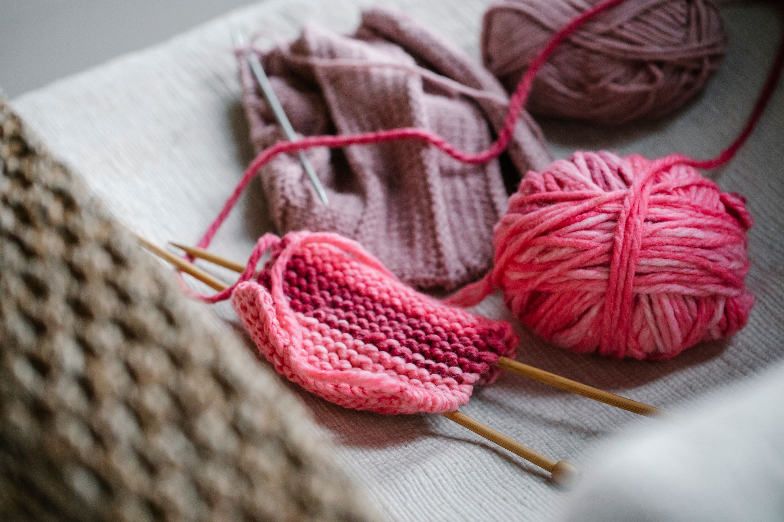 From above of knitted piece with bright pink yarn ball and knitting needles on sofa